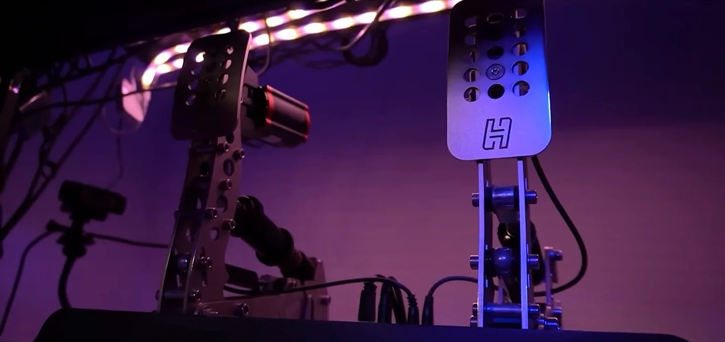 Heusinkveld load cell pedals seen from the side under purple LED lighting, the hardware that gives real brake pedal settings sim racing options for stiffness.
