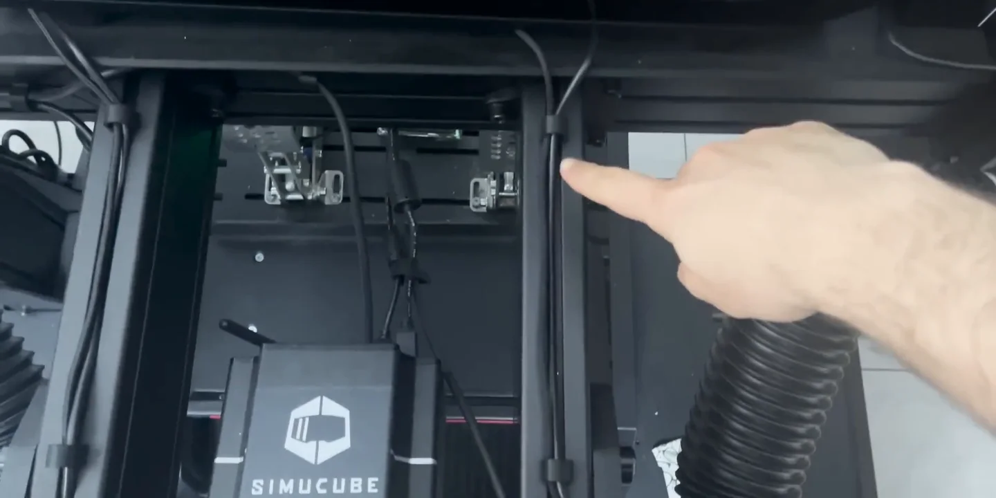 A finger pointing at a small black cable clip holding a cable in the T-slot of an aluminium profile rig, the cheapest of these sim racing accessories.