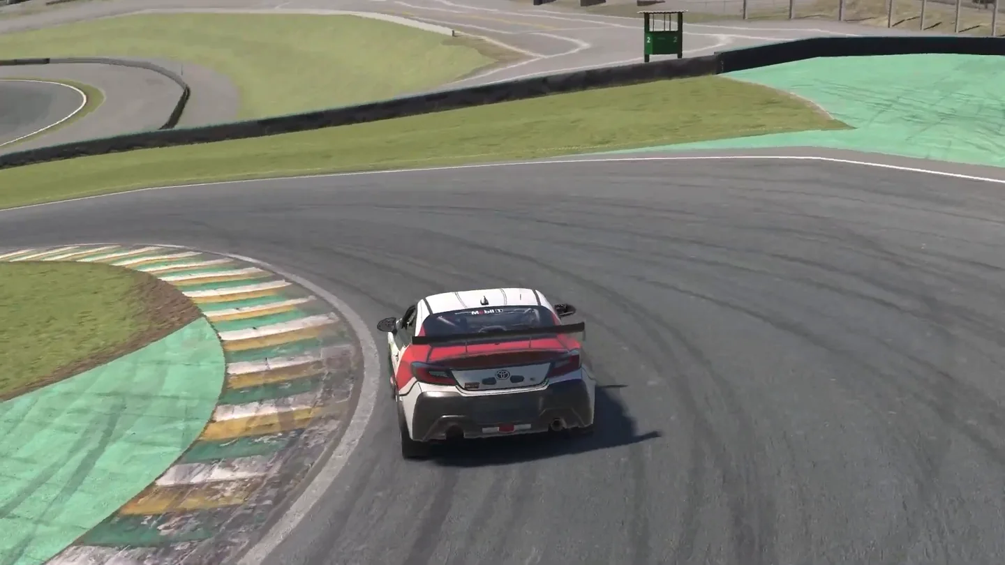 一台 Toyota GR86 在 Interlagos 入弯，模拟赛车走线在绿黄相间的路肩前还留有一个车身宽的沥青路面。