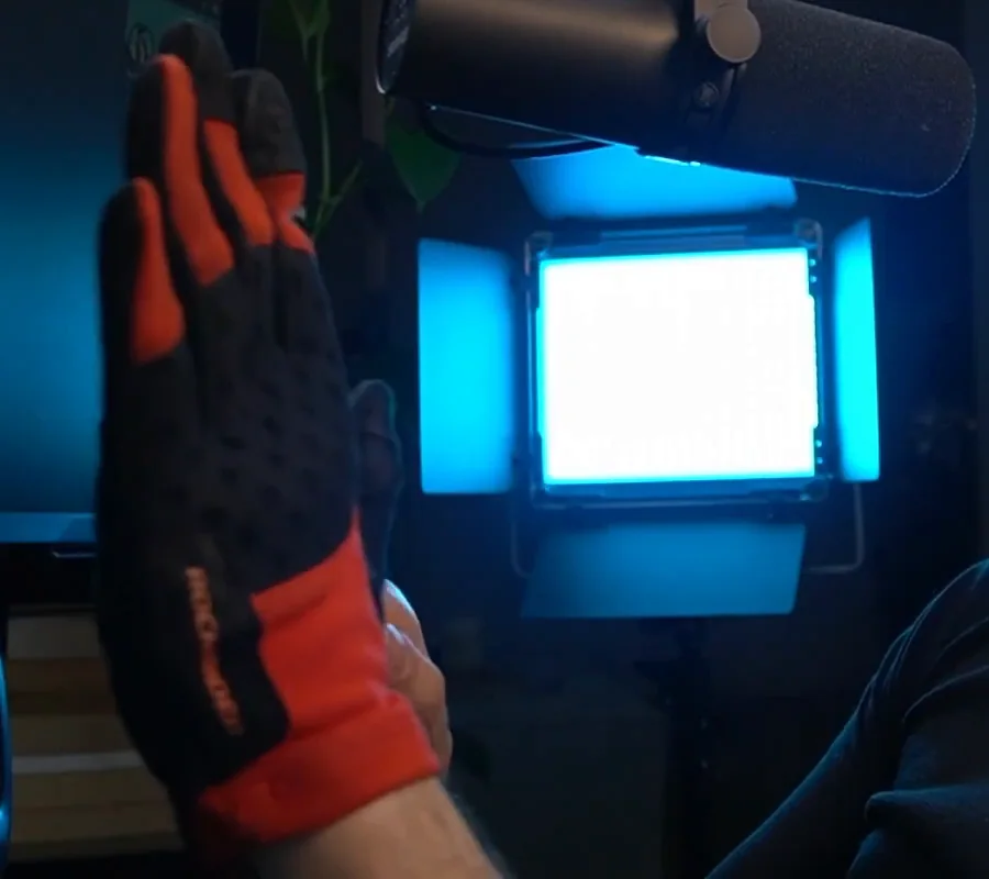 A red and black cycling glove worn on the hand and held up to the camera, the sub-ten-dollar pair that counts among these cheap sim racing upgrades.