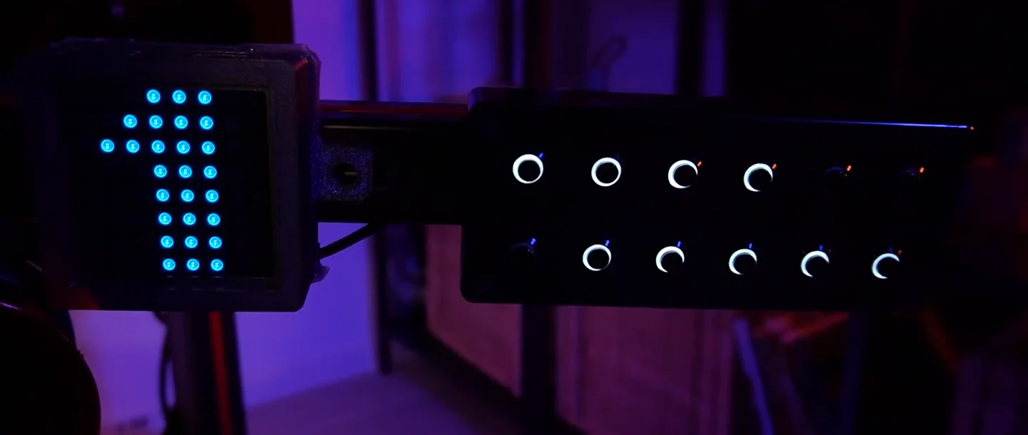 A simple button box with two rows of rotary dials and push buttons mounted on the rig next to an LED matrix lit up with a number one, one of the cheap sim racing upgrades that frees the wheel buttons for driving functions.