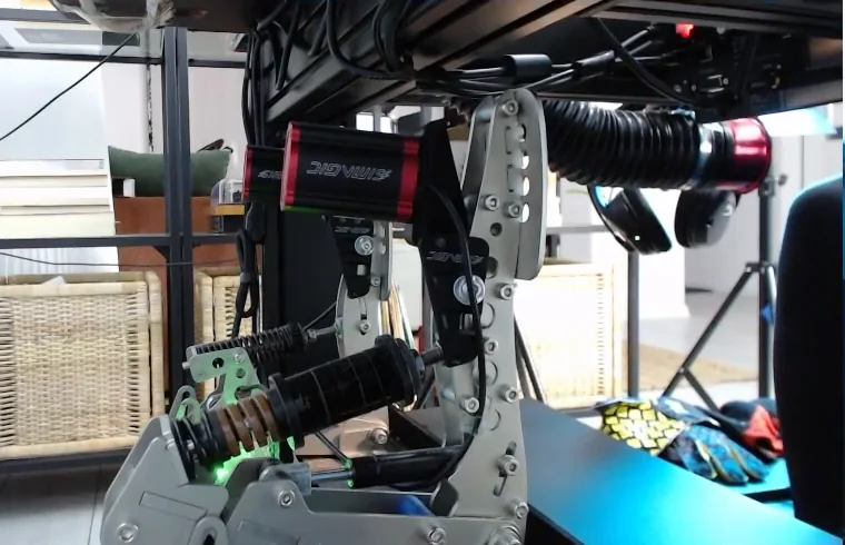 Red Simagic haptic reactors bolted to the brake and throttle arms of a metal pedal set, with the two-stage brake spring visible below, one of the cheap sim racing upgrades for pedal feedback.