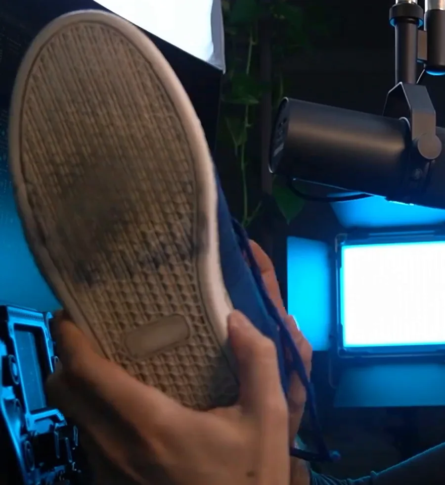 The thin, worn rubber sole of a blue lightweight flat shoe held up to the camera, the shoe recommended for stiffer pedals among cheap sim racing upgrades.