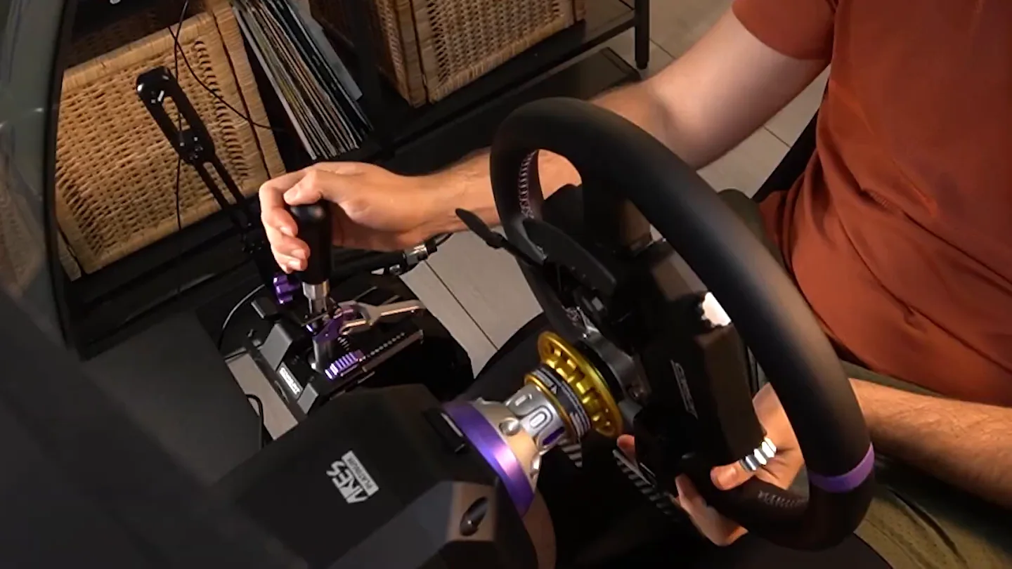 Conspit CHS shifter in a sim racing rig, the driver's hand on the knob, steering wheel in front and a handbrake lever beside the shifter