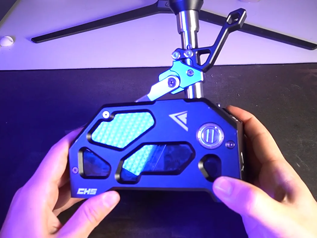 Conspit shifter held up to the camera, showing its side plate with the CHS logo and angular cut-outs under blue room lighting
