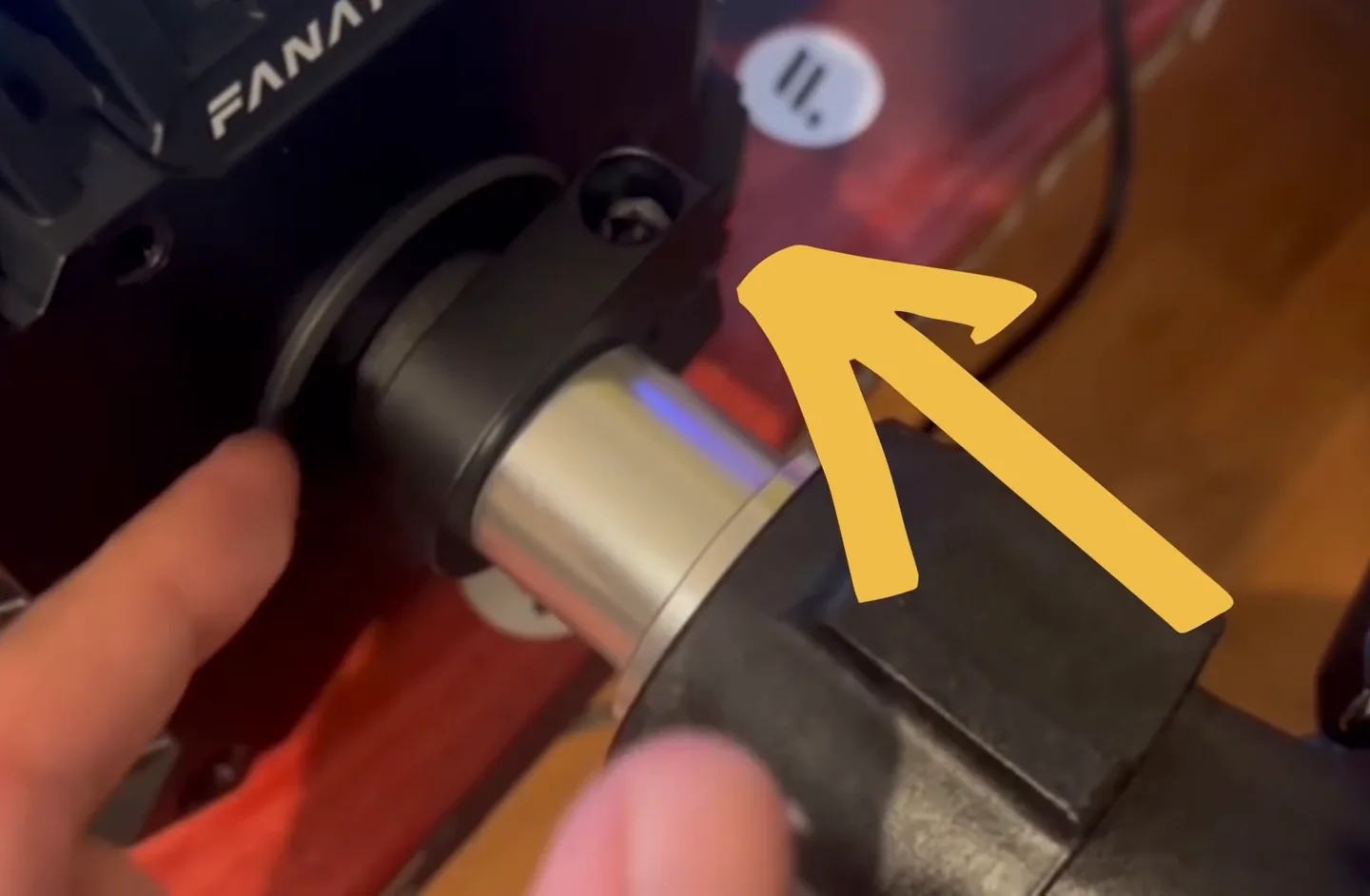 A yellow arrow points at the clamp on a Fanatec CSL DD base where the metal shaft emerges.