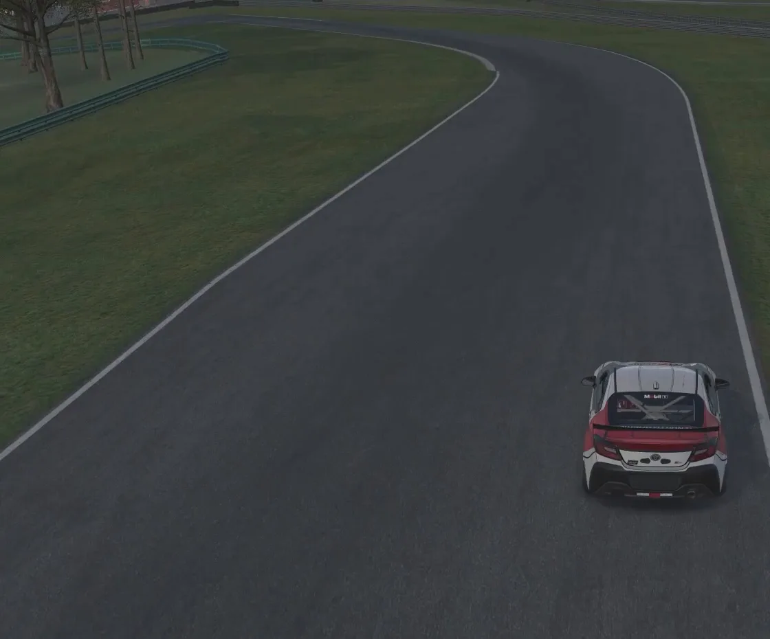 Chase-cam view of a red-and-white race car on the right-hand side of the track approaching a long left-hand bend, opening the compromised-corner section of this guide to racing corner types.