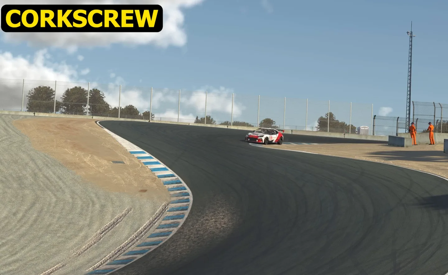 One of the racing corner types labelled on track as the corkscrew: a red-and-white car at the far brow where the tarmac falls away, the road dropping toward the camera and swinging left past blue-and-white kerbs.