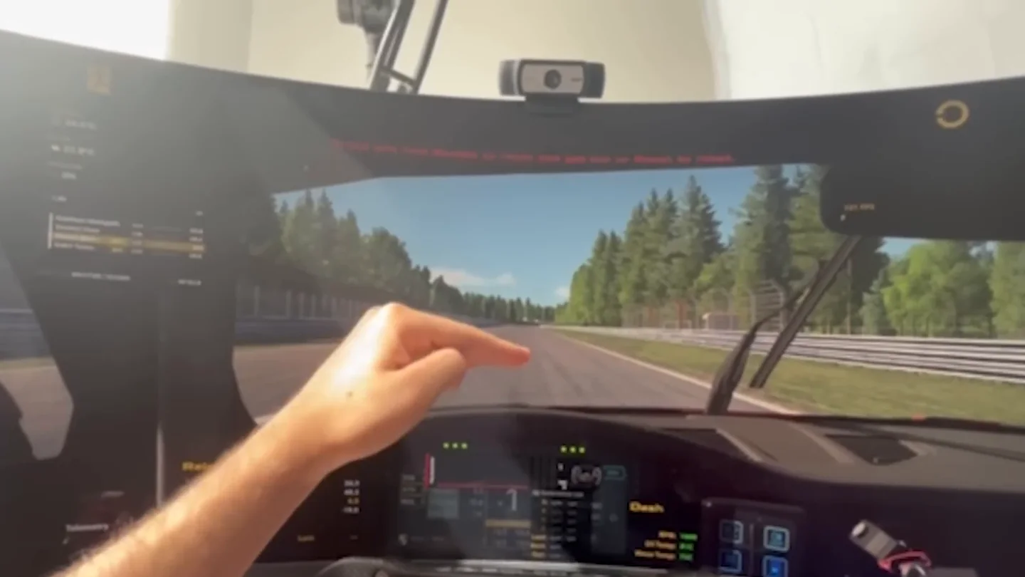 A hand pointing up at the webcam clipped to the top edge of the monitor, mounted above the driver's eye line for the sim racing head tracking test.