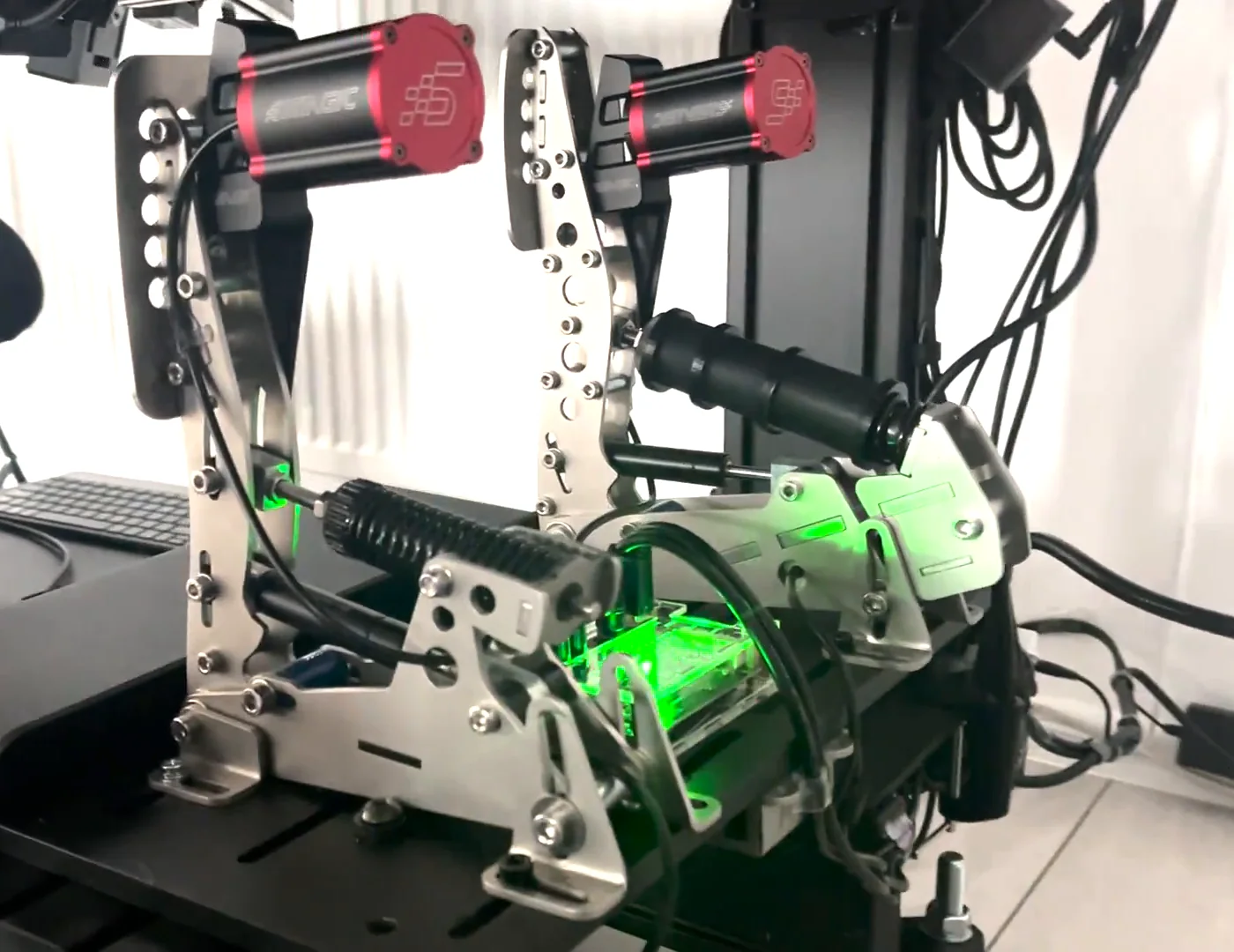 Two Simagic reactors fitted to both Heusinkveld pedals on a rig, the finished Simagic haptic reactor Heusinkveld mount with the control box lit green between them.