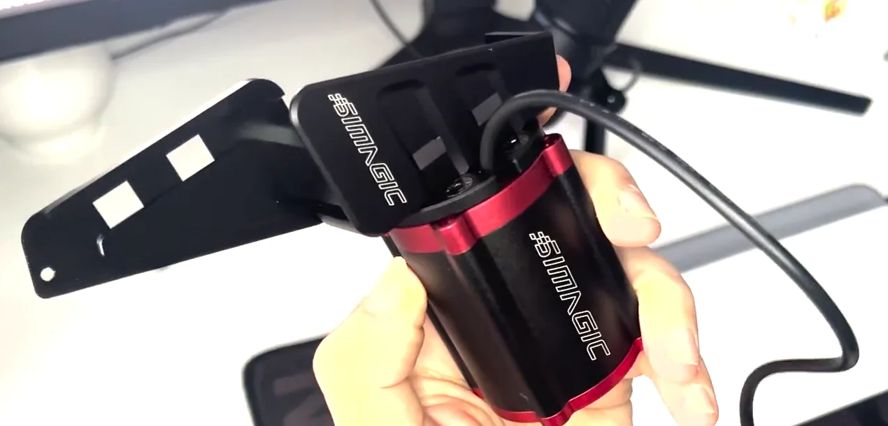 A Simagic reactor held in one hand with its two-part bracket assembled at an angle rather than flush, the orientation used for a Simagic haptic reactor Heusinkveld mount.