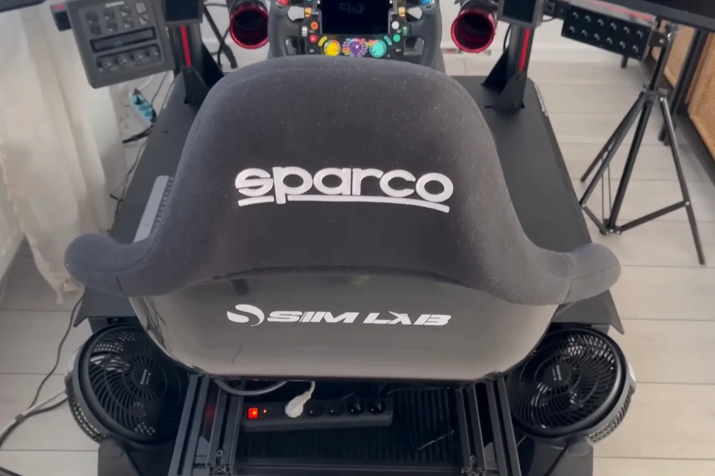 Top-down view of a Sim-Lab rig with a Sparco seat and a floor fan on each side of the seat base, the cooling arrangement behind these SimHub bass shaker settings.